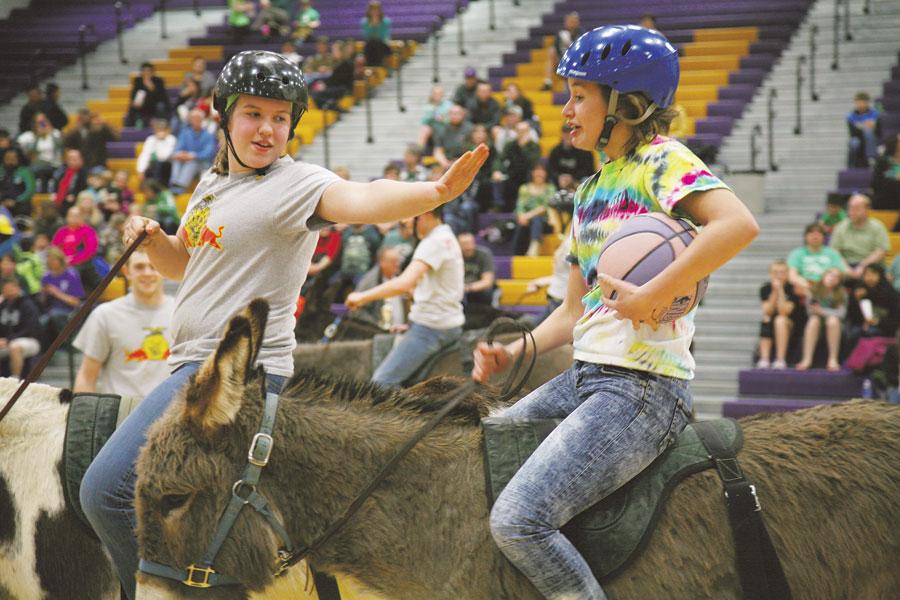 Sophomore Savannah Brass and junior Bethany Symonds battle for the ball on their donkeys during Donkey Basketball on March 17.