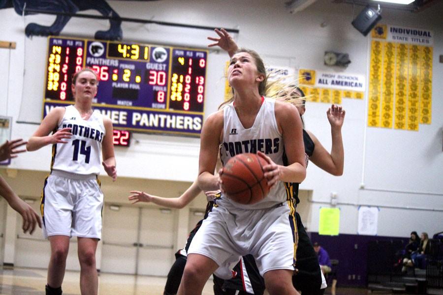 Senior Amira Chandler looks up to the basket trying to score as junior Maddi Hallberg watches from behind.